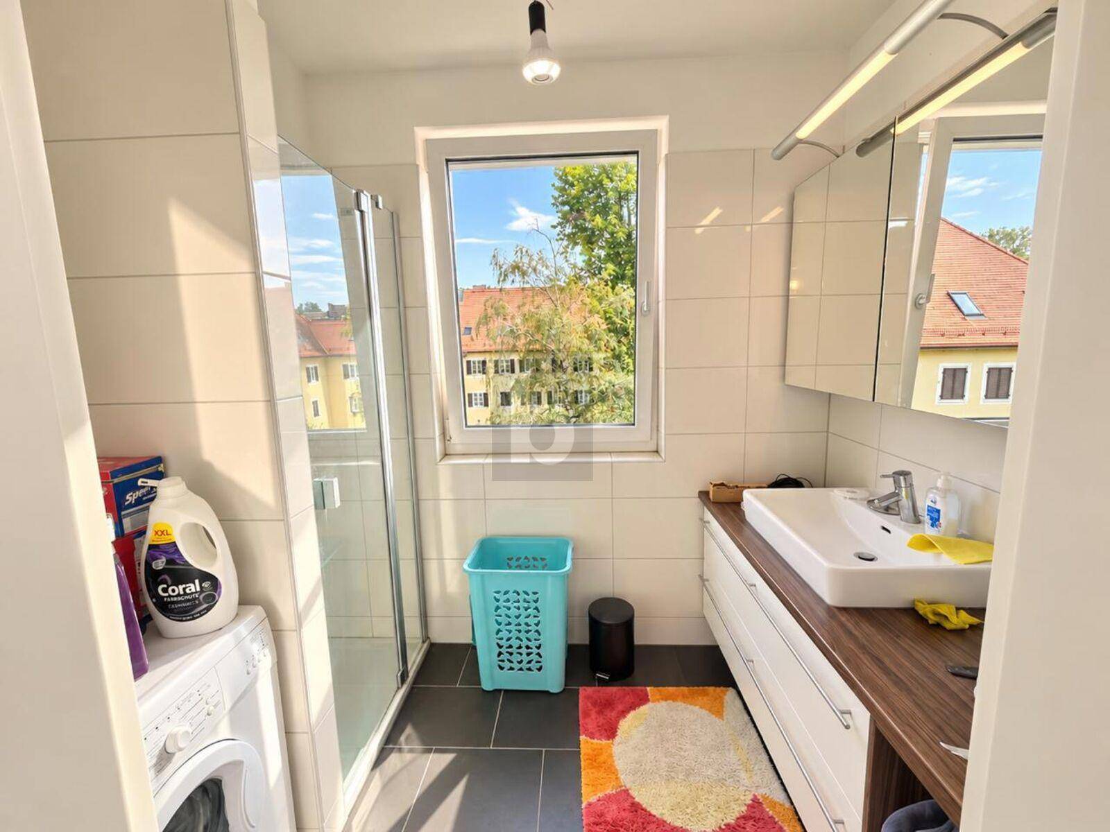 Modernes Badezimmer mit Dusche, Fenster und Waschmaschinenanschluss.