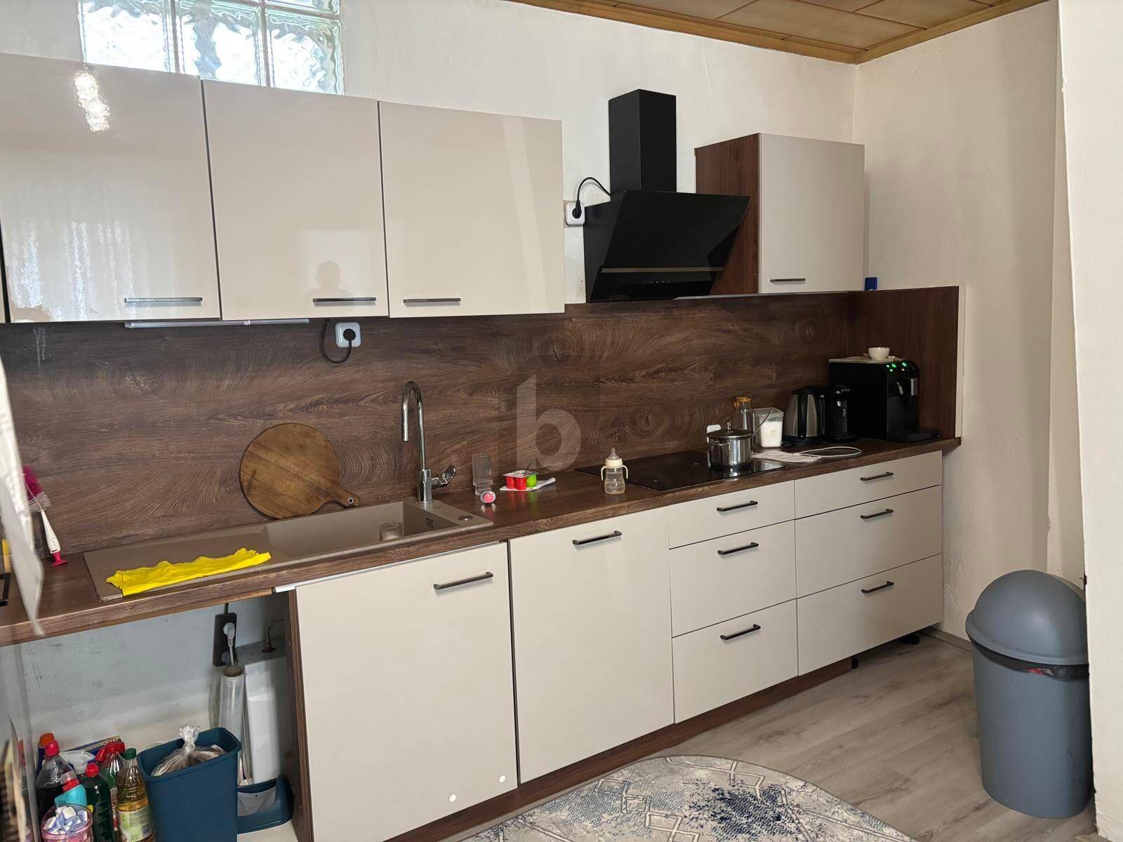 Moderne Küche mit hellbeigen Schränken, Holzoptik-Rückwand und integrierten schwarzen Geräten.