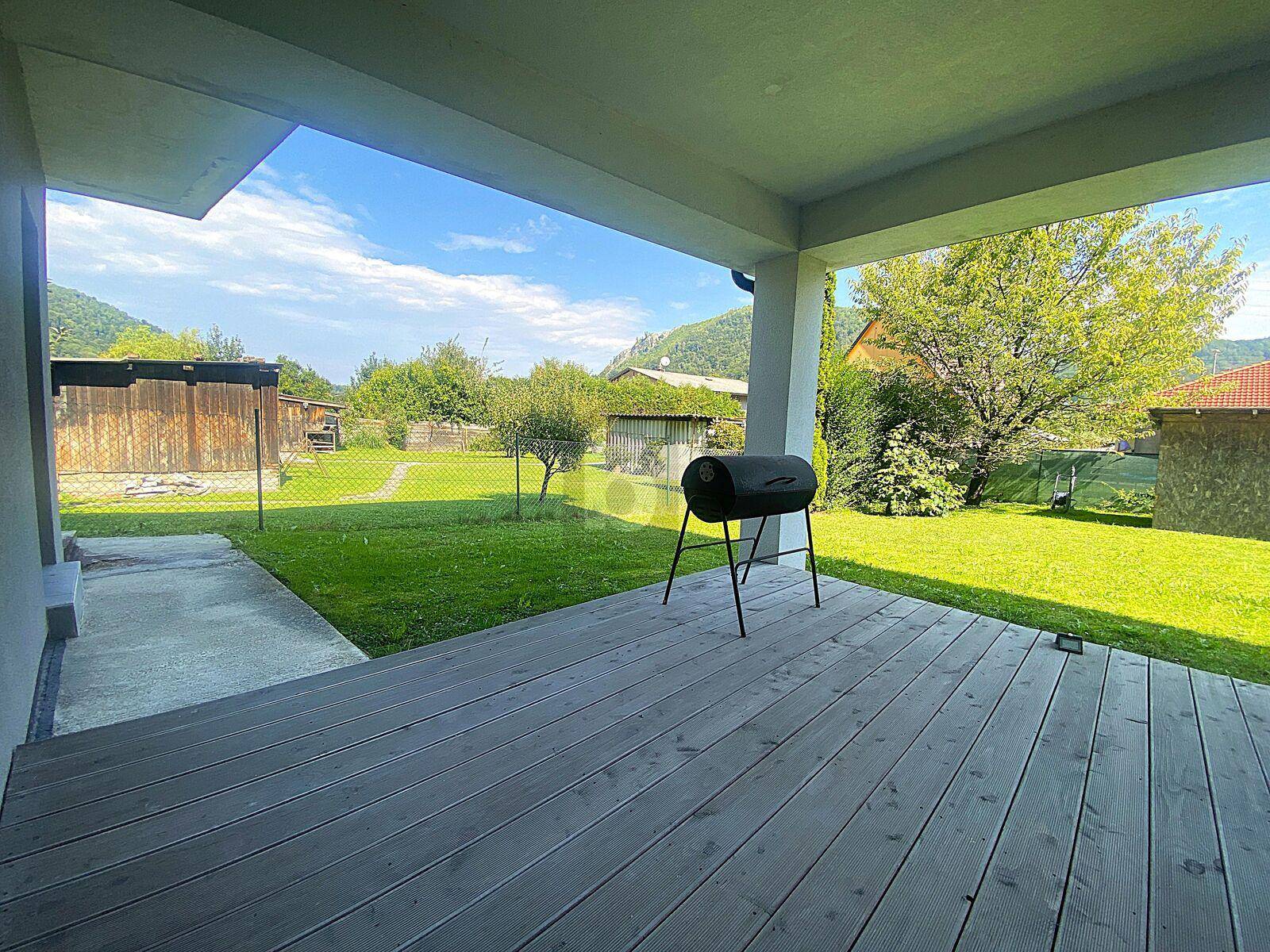 Überdachte Holzterrasse mit Grill und Blick auf den grünen Gartenbereich.