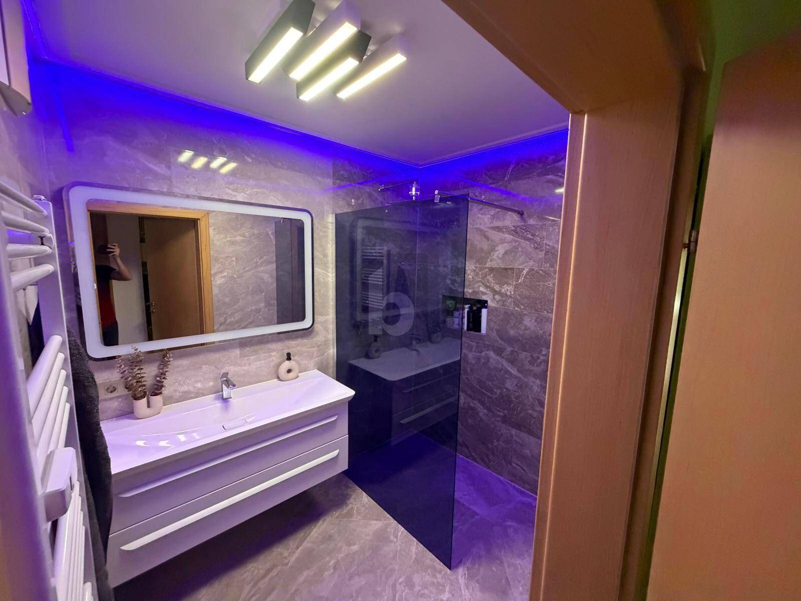 Modernes Badezimmer mit begehbarer Dusche, Einzelwaschbecken und stilvoller LED-Beleuchtung.