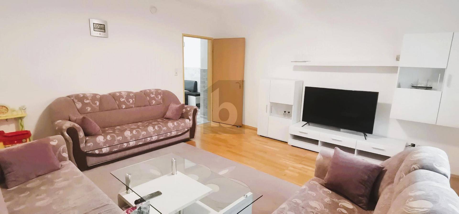 Helles Wohnzimmer mit bequemen Sofas, einem Fernseher und hellem Holzparkettboden.