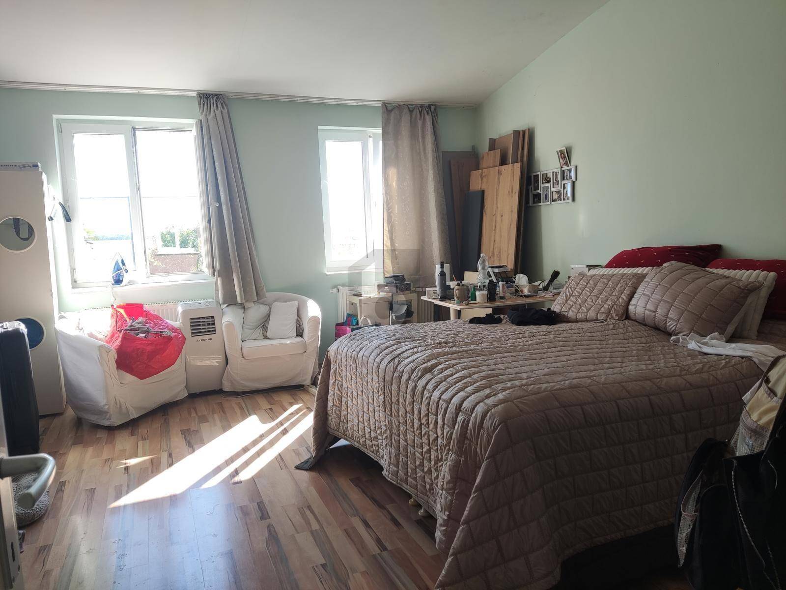 Helles Schlafzimmer mit Holzboden, großem Bett und Fenstern, die viel Tageslicht hereinlassen.