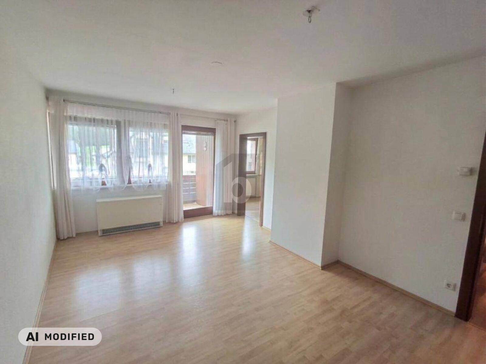 Helles, leeres Wohnzimmer mit Laminatboden, großen Fenstern und Zugang zum Balkon.