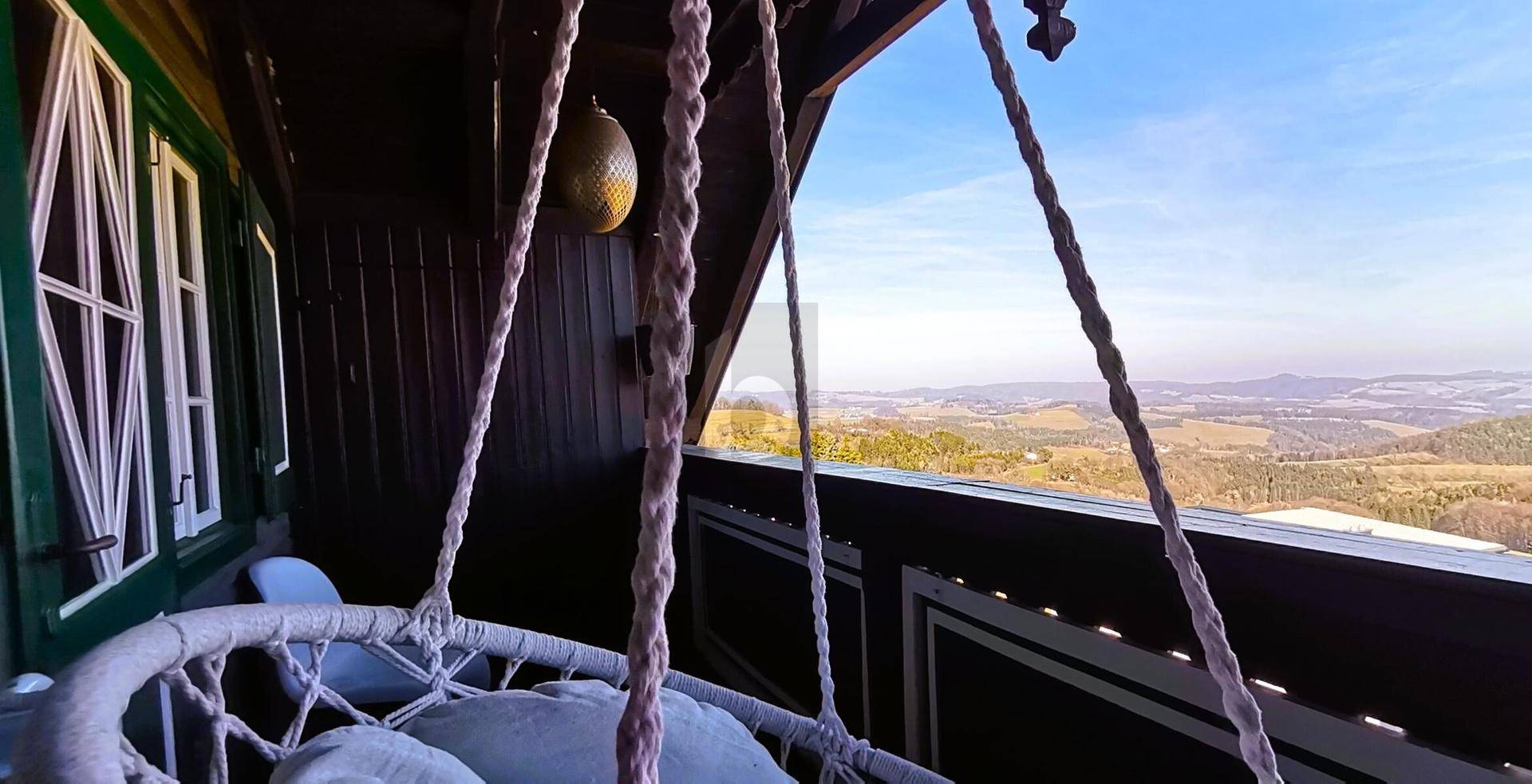 Überdachter Balkon mit Hängesessel und weitem Blick über die hügelige Winterlandschaft.