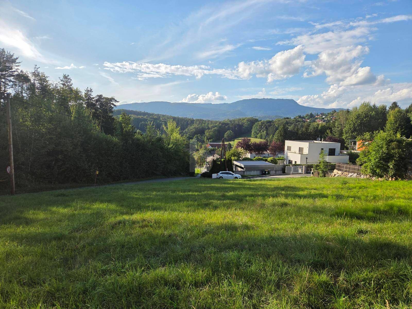 Idyllische Landschaft mit grünen Wiesen, bewaldeten Hügeln und einem modernen Haus im Hintergrund.