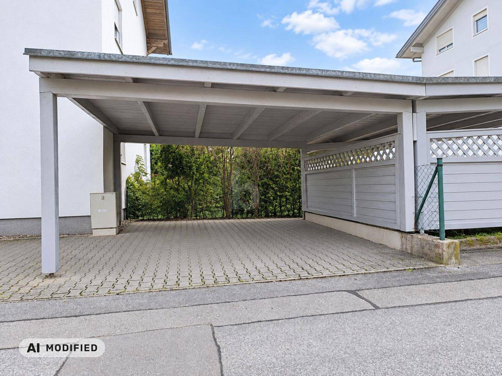 Überdachter Carport mit gepflastertem Stellplatz für Fahrzeuge.