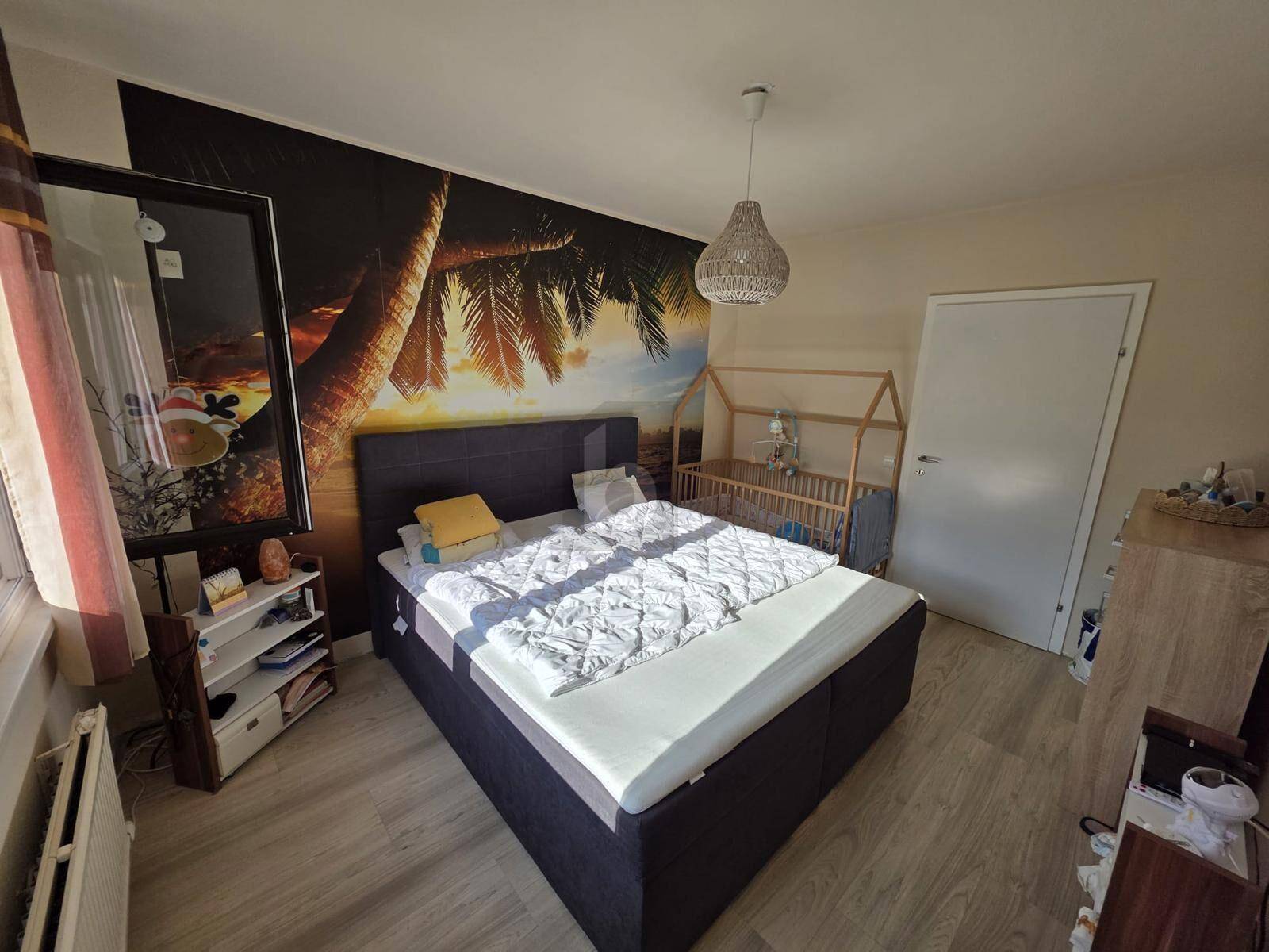 Gemütliches Schlafzimmer mit Doppelbett, Babybett und einer auffälligen tropischen Wandtapete.