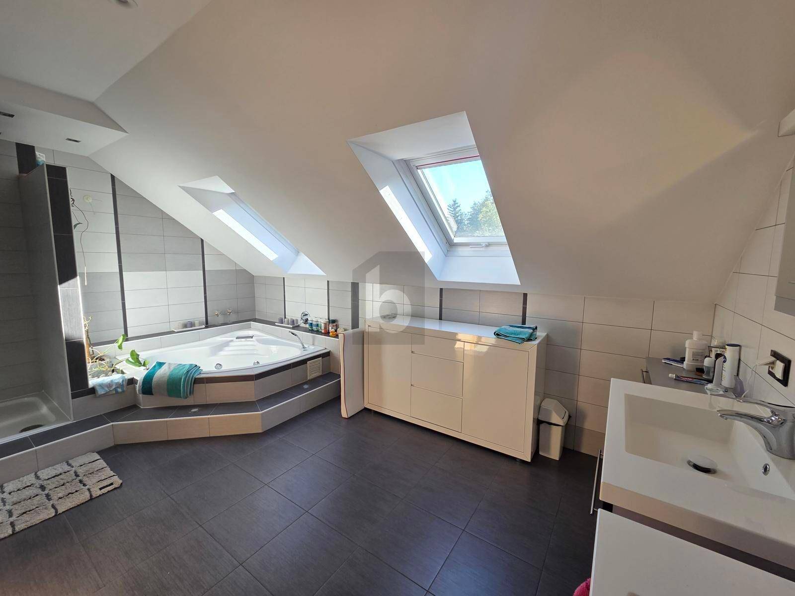 Geräumiges Badezimmer im Dachgeschoss mit Whirlpool, Dusche, Waschbecken und Dachfenstern.