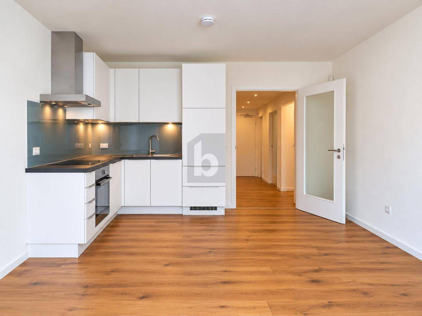 Moderne Küchenzeile mit weißen Schränken, dunkler Arbeitsplatte und Holzboden in offenem Raum.