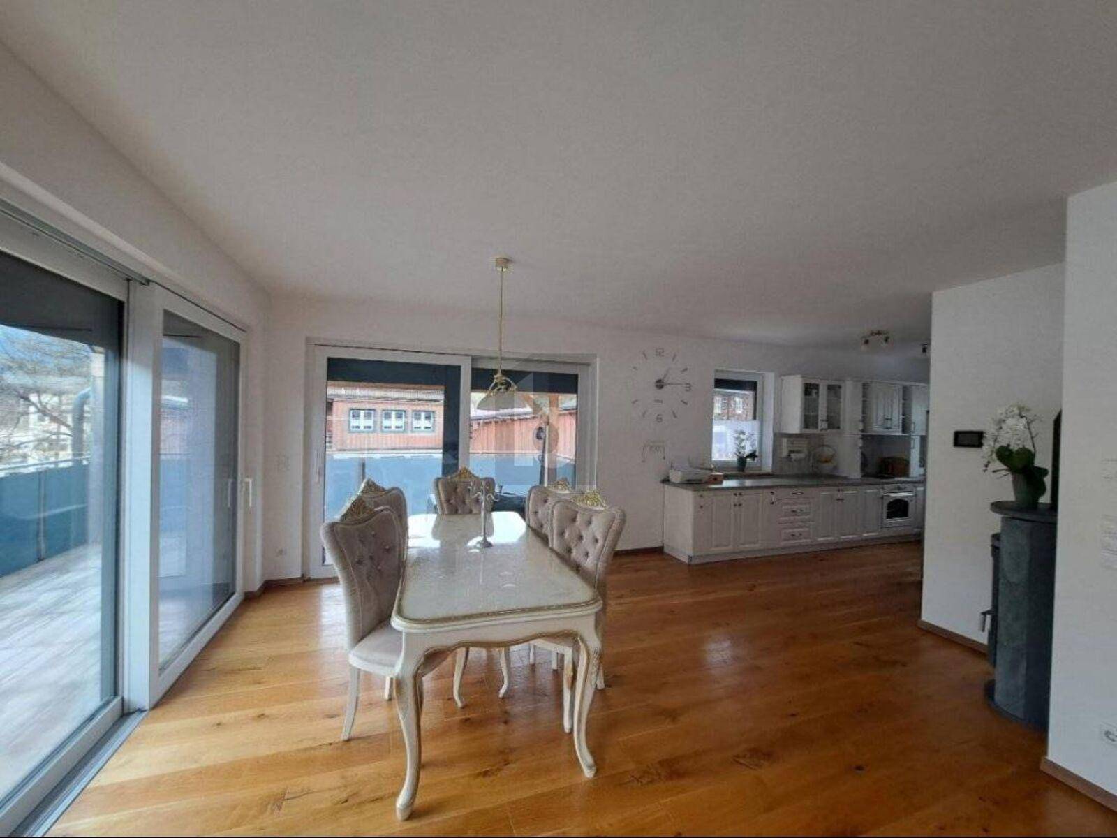 Heller offener Wohn-Essbereich mit Holzboden, elegantem Esstisch und Zugang zum Balkon.