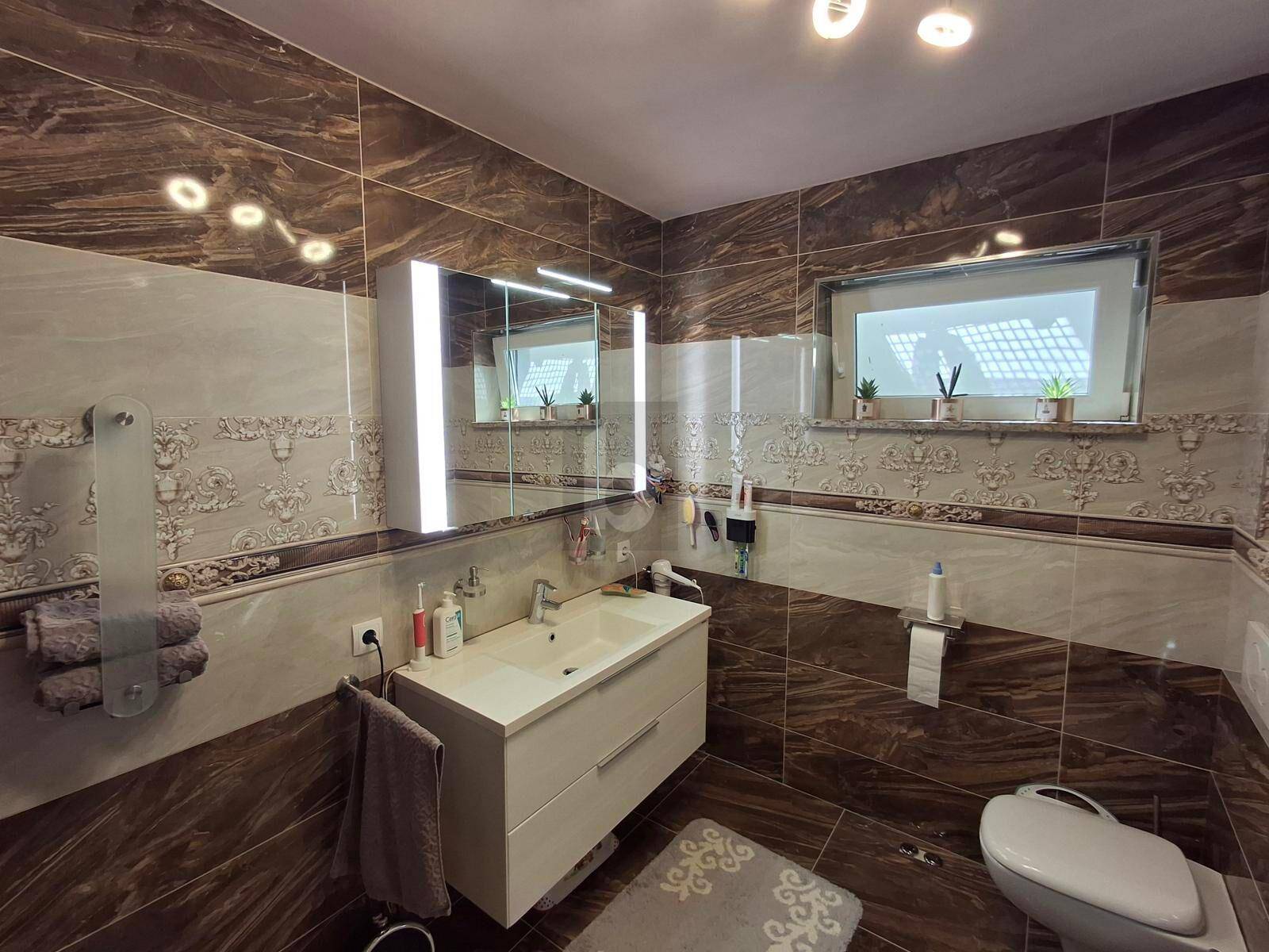 Modernes Badezimmer mit braunen Fliesen, Doppelwaschbecken und Spiegelschrank über dem Waschtisch.
