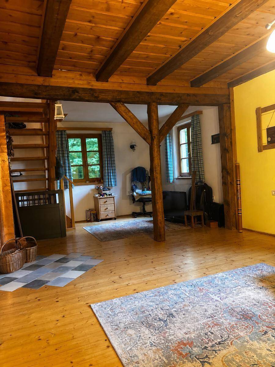 Rustikaler Wohnbereich mit sichtbaren Holzbalken, Holzfußboden und einer Holztreppe.