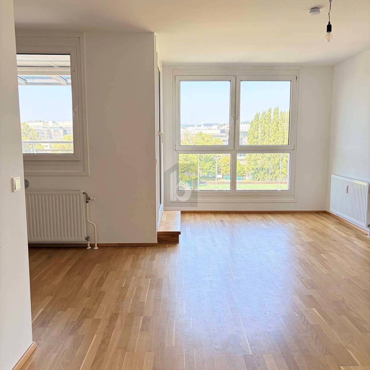 Geräumiger, heller Raum mit Holzparkettboden und großen Fenstern mit Blick ins Grüne.