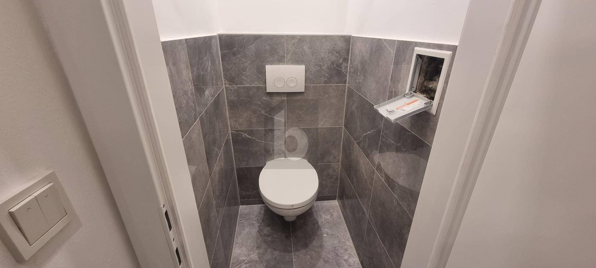 Modernes Gäste-WC mit grauen Fliesen an Wänden und Boden sowie einer wandhängenden Toilette.