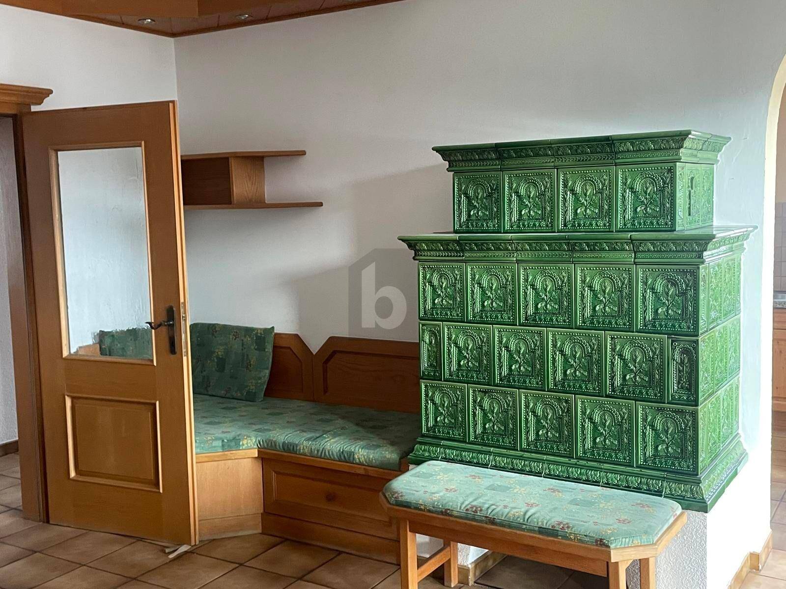 Wohnbereich mit einem markanten grünen Kachelofen, einer Holzsitzbank und traditionellem Charme.