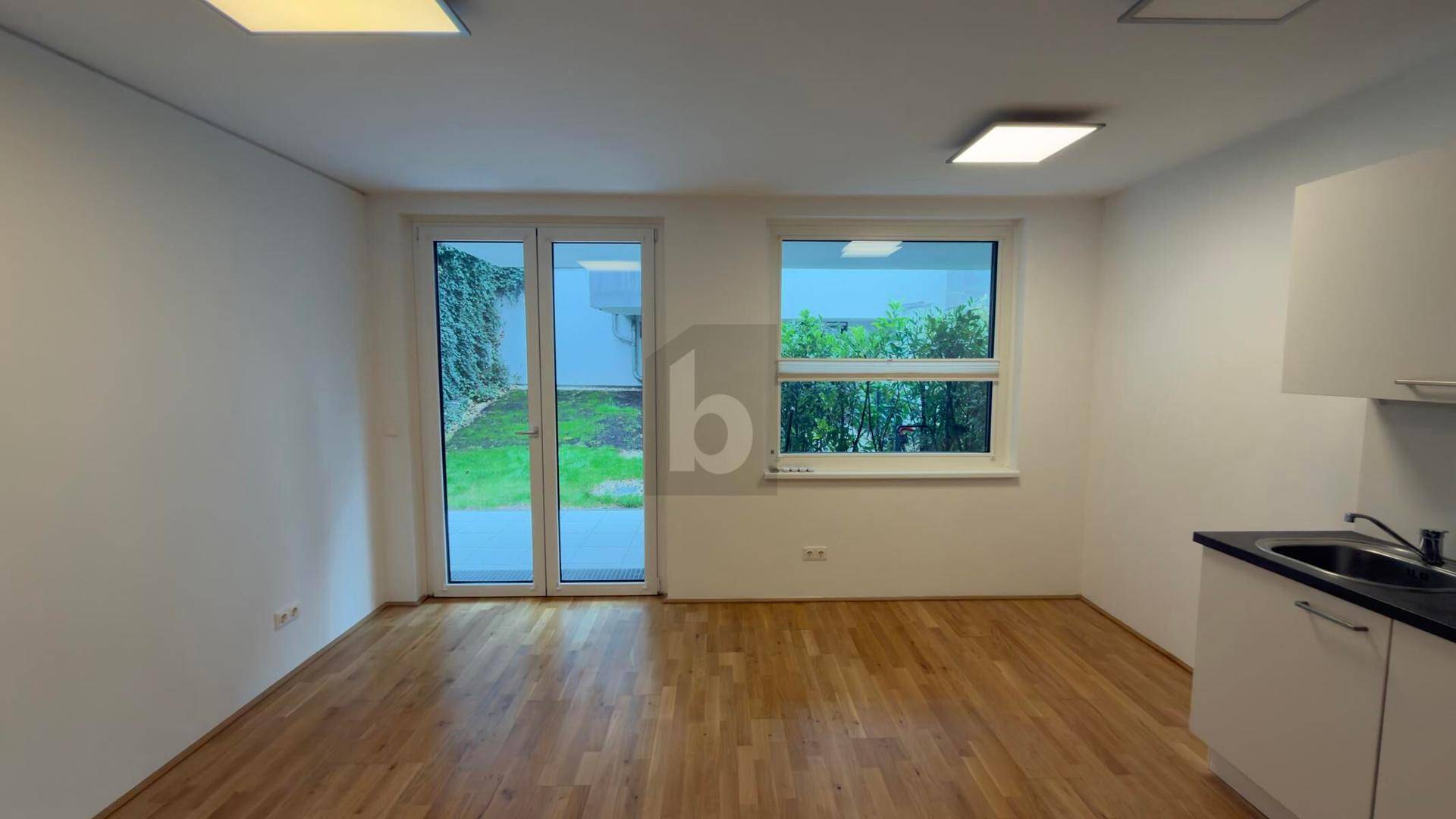 Heller Raum mit Holzboden, großen Fenstern und Zugang zu einem kleinen Gartenbereich.
