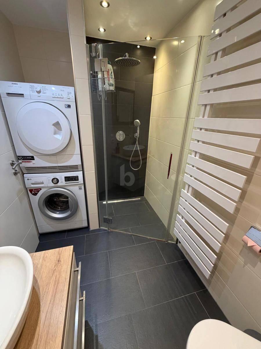 Badezimmer mit moderner begehbarer Dusche, Regendusche und integrierter Waschmaschine.