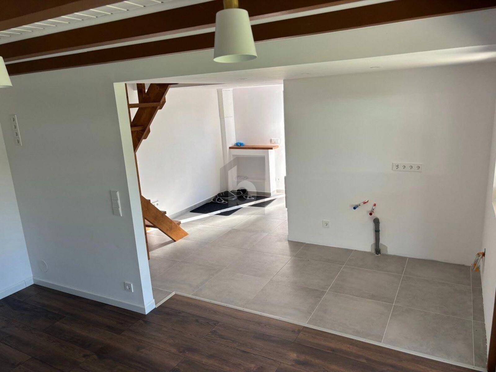 Offener Wohnbereich mit Treppe, Fliesenboden und vorbereitetem Küchenbereich.
