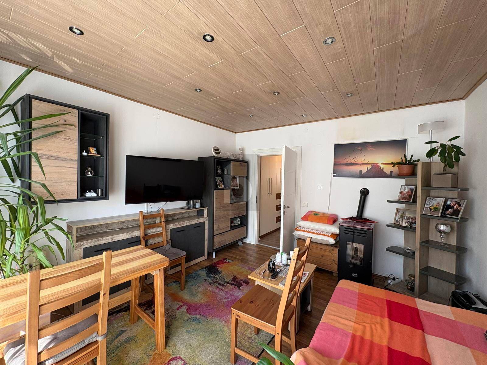 Gemütliches Wohnzimmer mit Holzbalkendecke, farbenfrohem Teppich und Kaminofen.