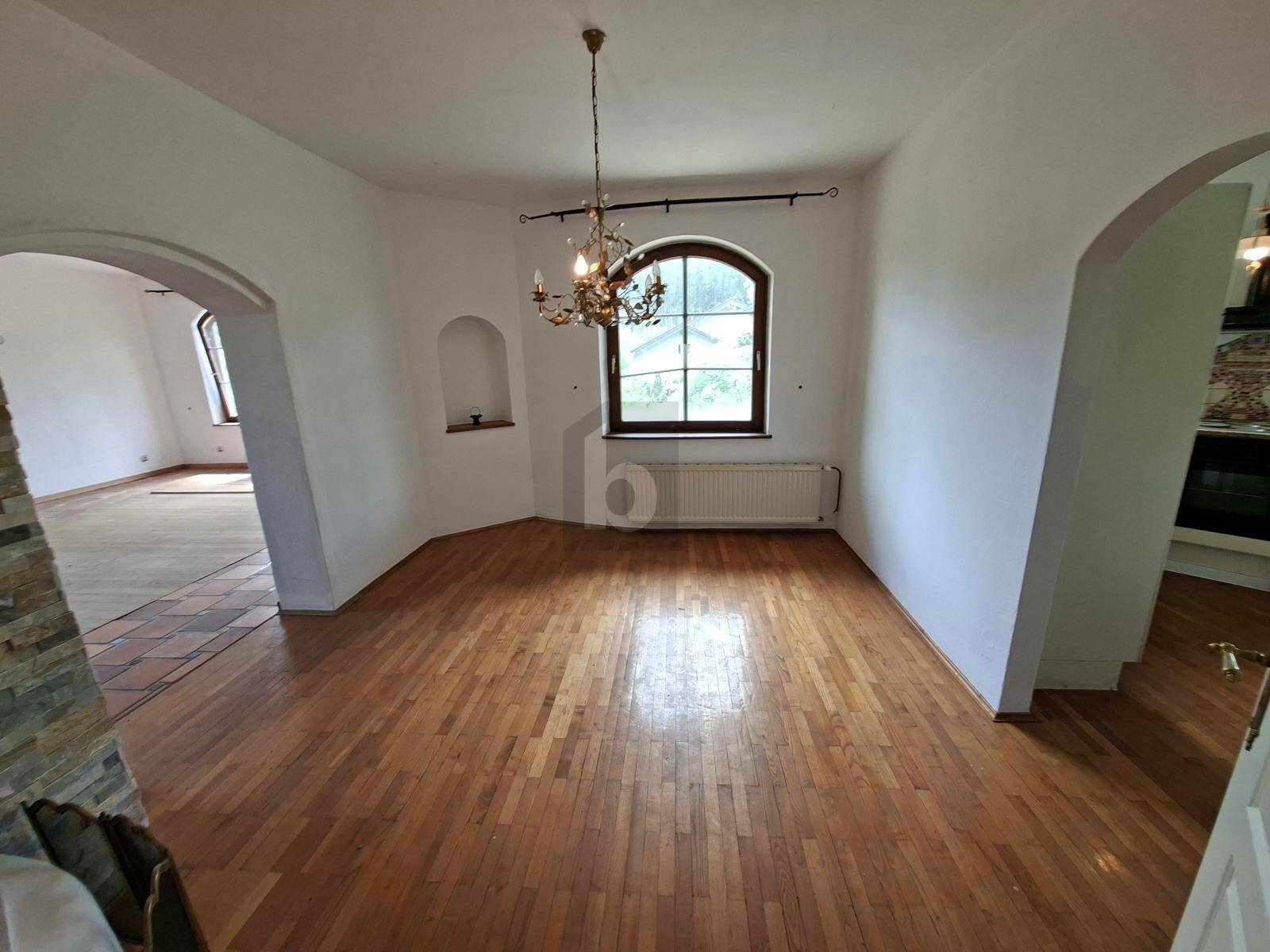 Helles Wohnzimmer mit Holzboden, Kronleuchter und einem großen Rundbogenfenster mit Blick auf die Landschaft.