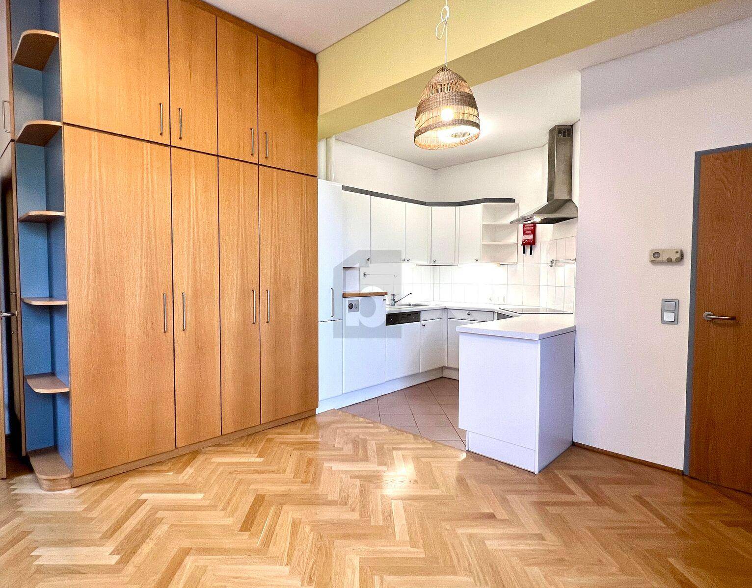 Offener Wohnbereich mit Einbauküche, Holzschrank und Fischgrätparkettboden.