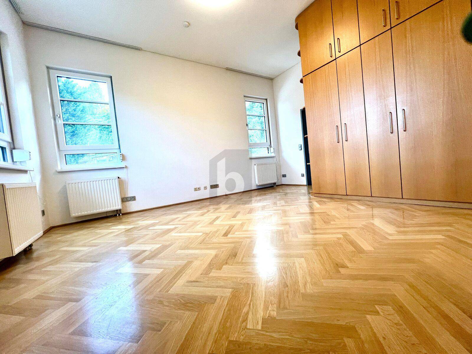 Geräumiger Wohnraum mit hellem Fischgrätparkett, großen Fenstern und Einbauschrank.