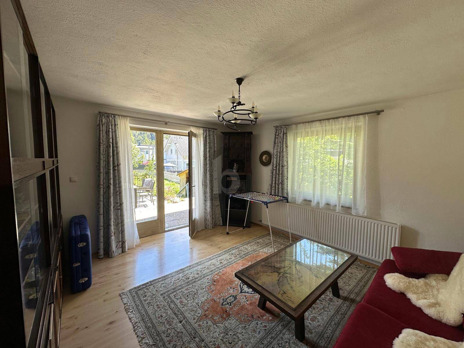 Heller Wohnraum mit Teppich, Couchtisch und Ausgang zu einer sonnigen Terrasse.