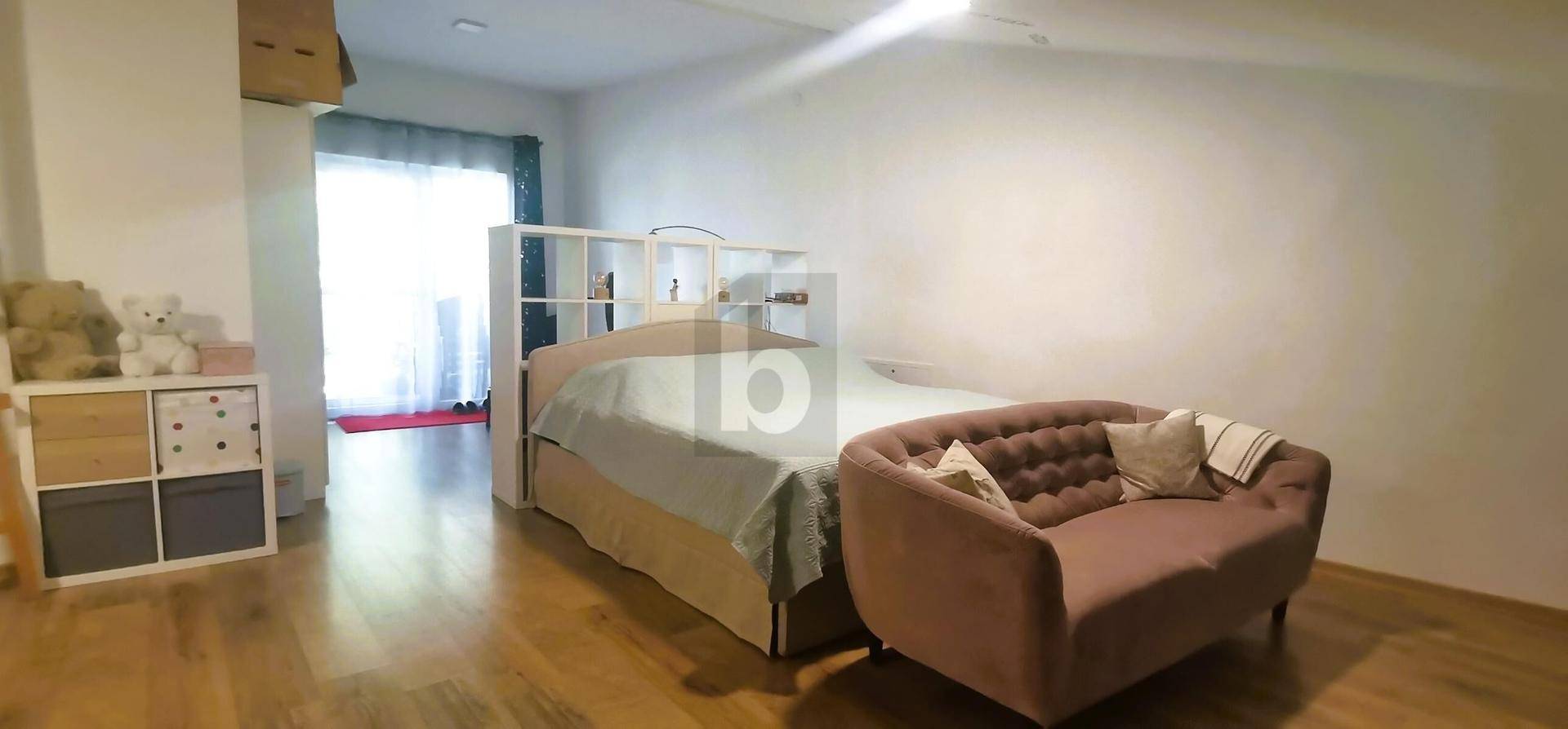 Schlafzimmer mit Bett, kleinem Sofa und großem Fenster für viel Tageslicht.
