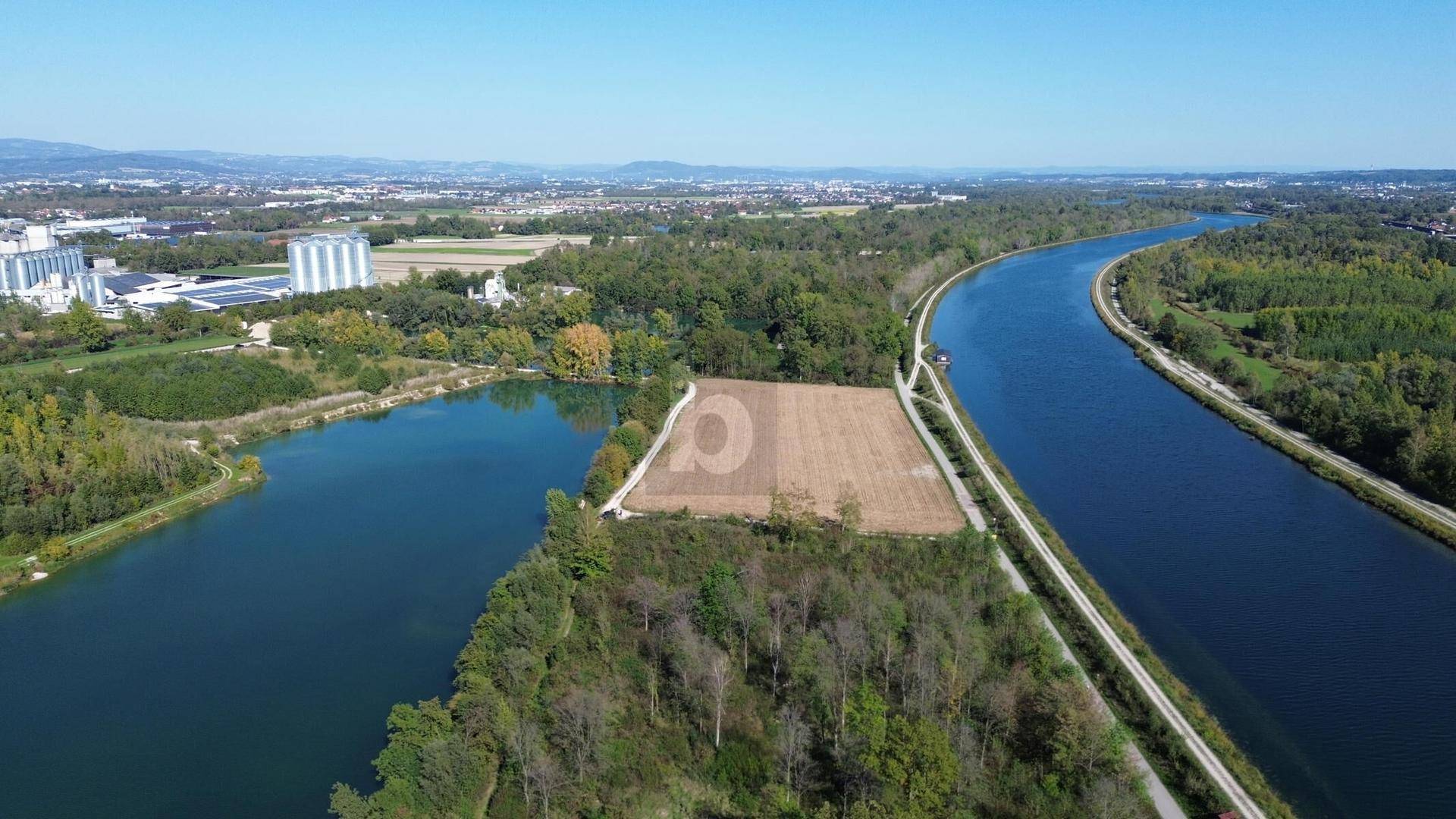 Weitläufige Luftaufnahme eines Grundstücks mit Wasserläufen, Feldern und einer Stadt in der Ferne unter blauem Himmel.