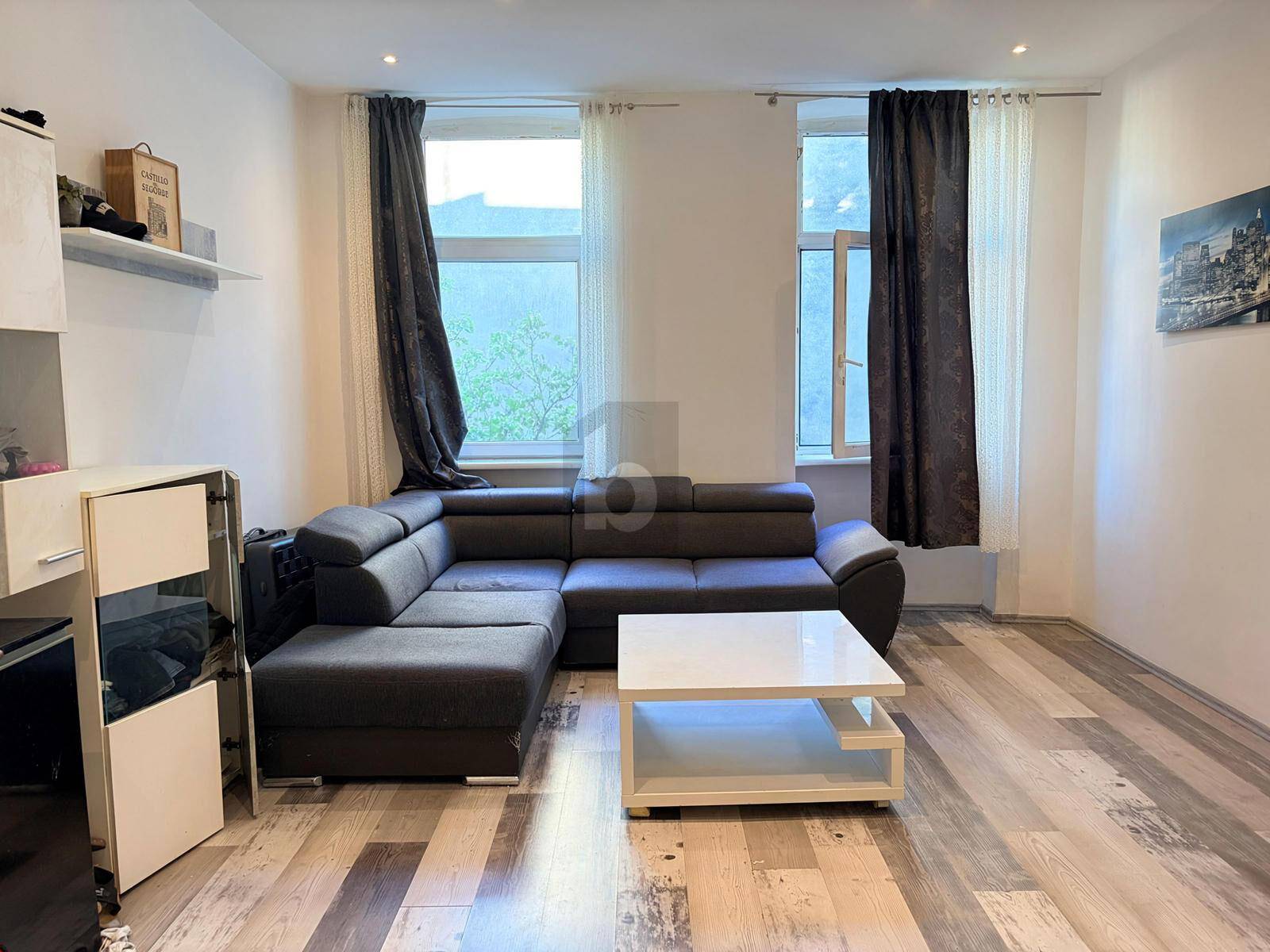 Gemütliches Wohnzimmer mit dunklem Ecksofa, hellem Couchtisch und Laminatboden.