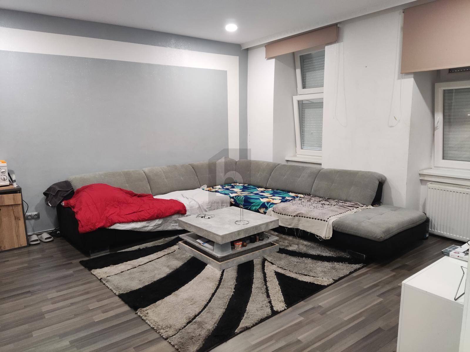 Gemütliches Wohnzimmer mit großem Ecksofa, Teppich und Laminatboden, gut beleuchtet durch Fenster.