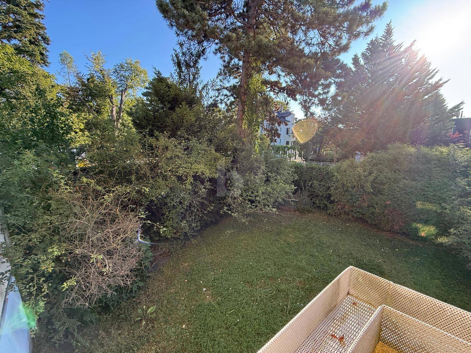 Blick von einem Balkon oder einer Terrasse auf einen gepflegten Gartenbereich mit üppiger grüner Bepflanzung und Bäumen.