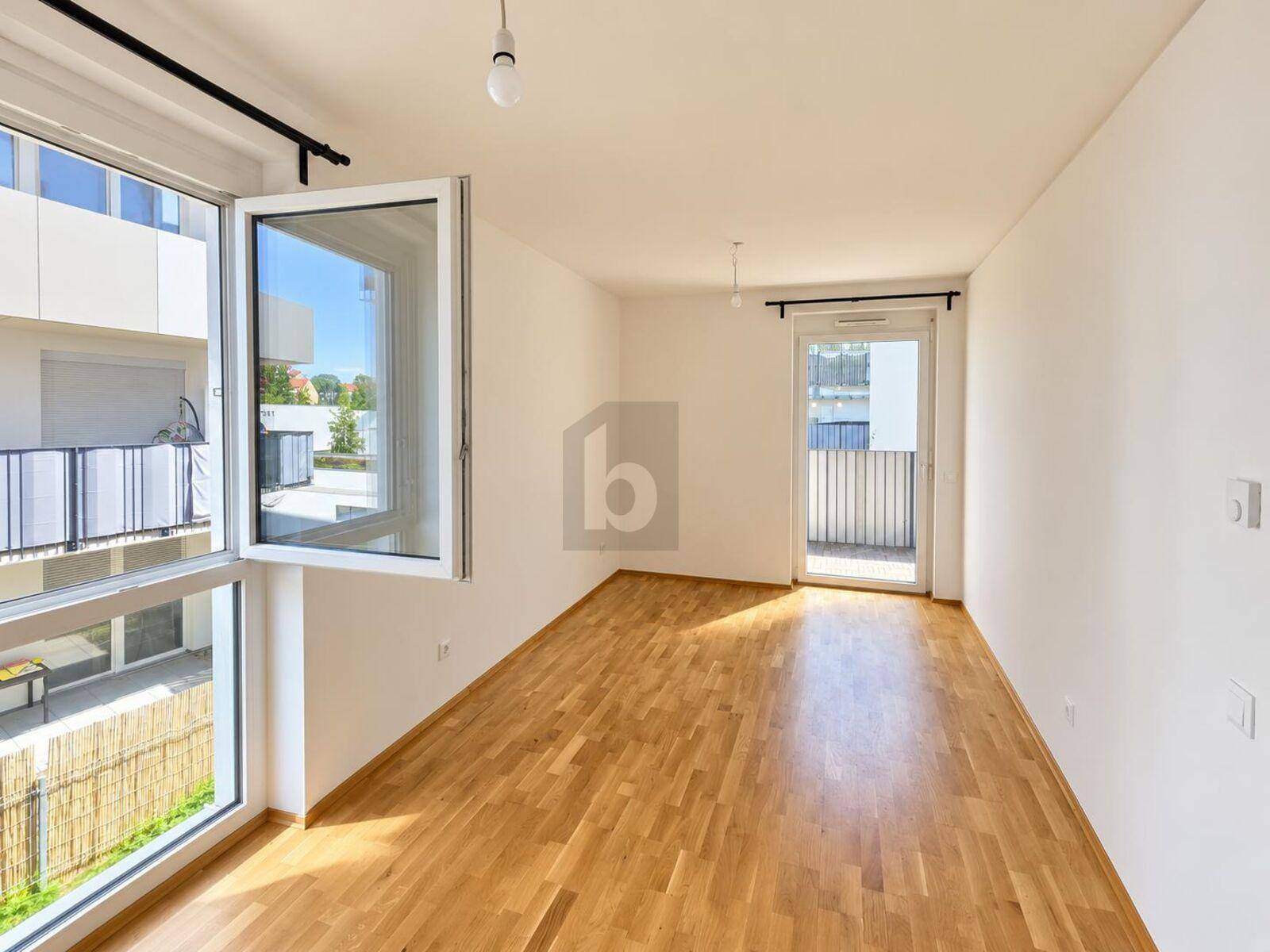 Heller Raum mit Parkettboden, großen Fenstern und Zugang zu einem Balkon.
