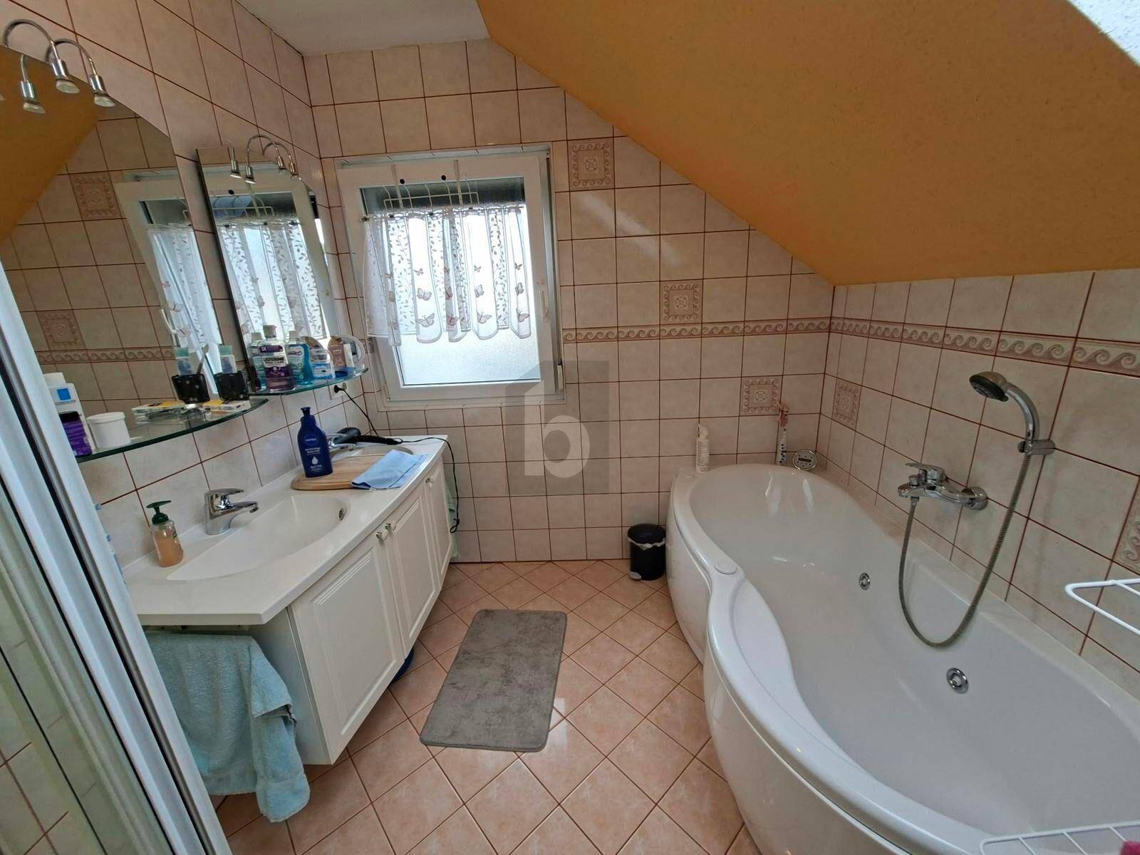 Badezimmer mit Eckbadewanne, Waschbecken und Fenster unter einer Dachschräge.