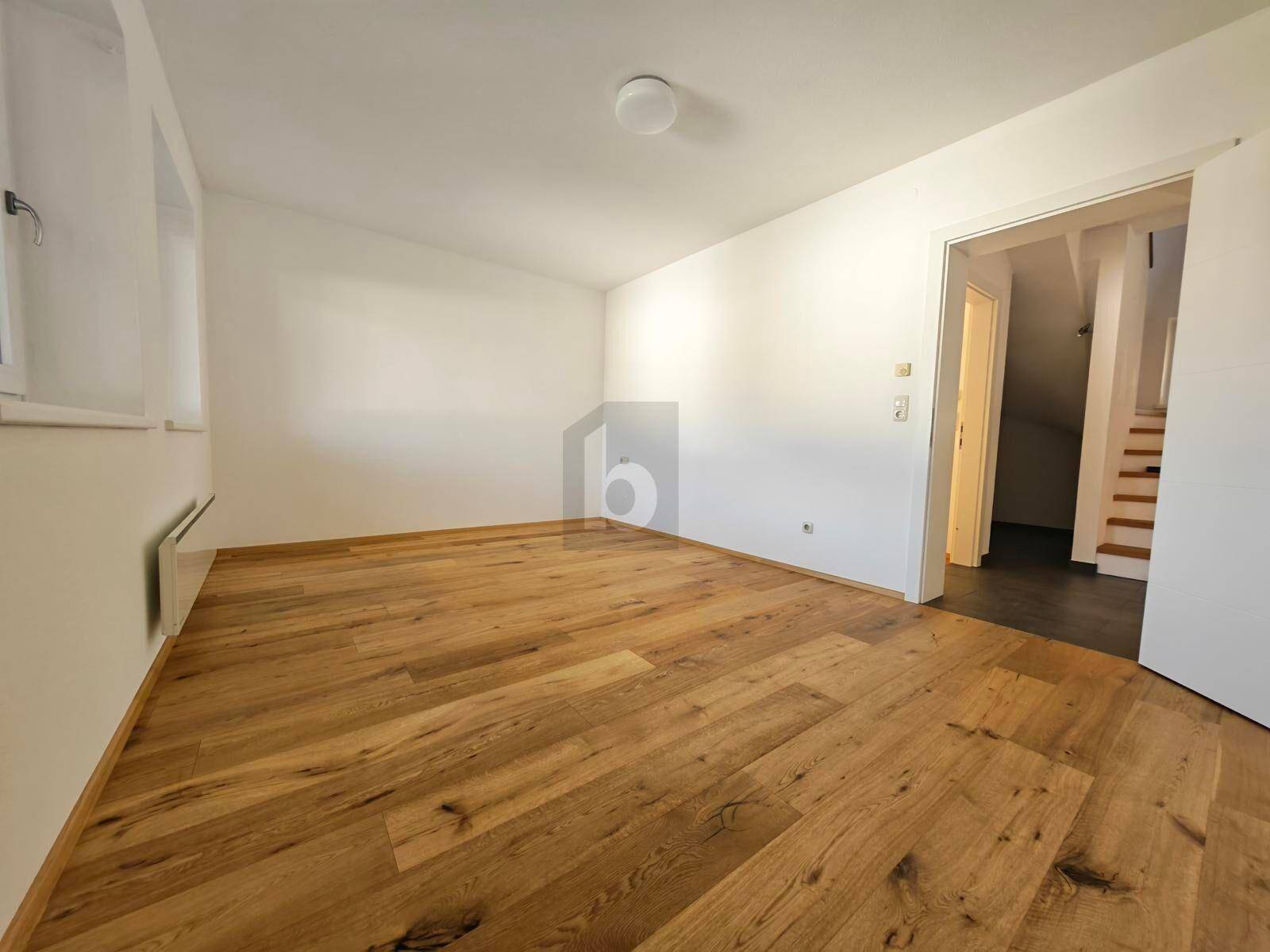 Helles Schlafzimmer mit Holzboden und weiß gestrichenen Wänden, angrenzend an einen Flur.