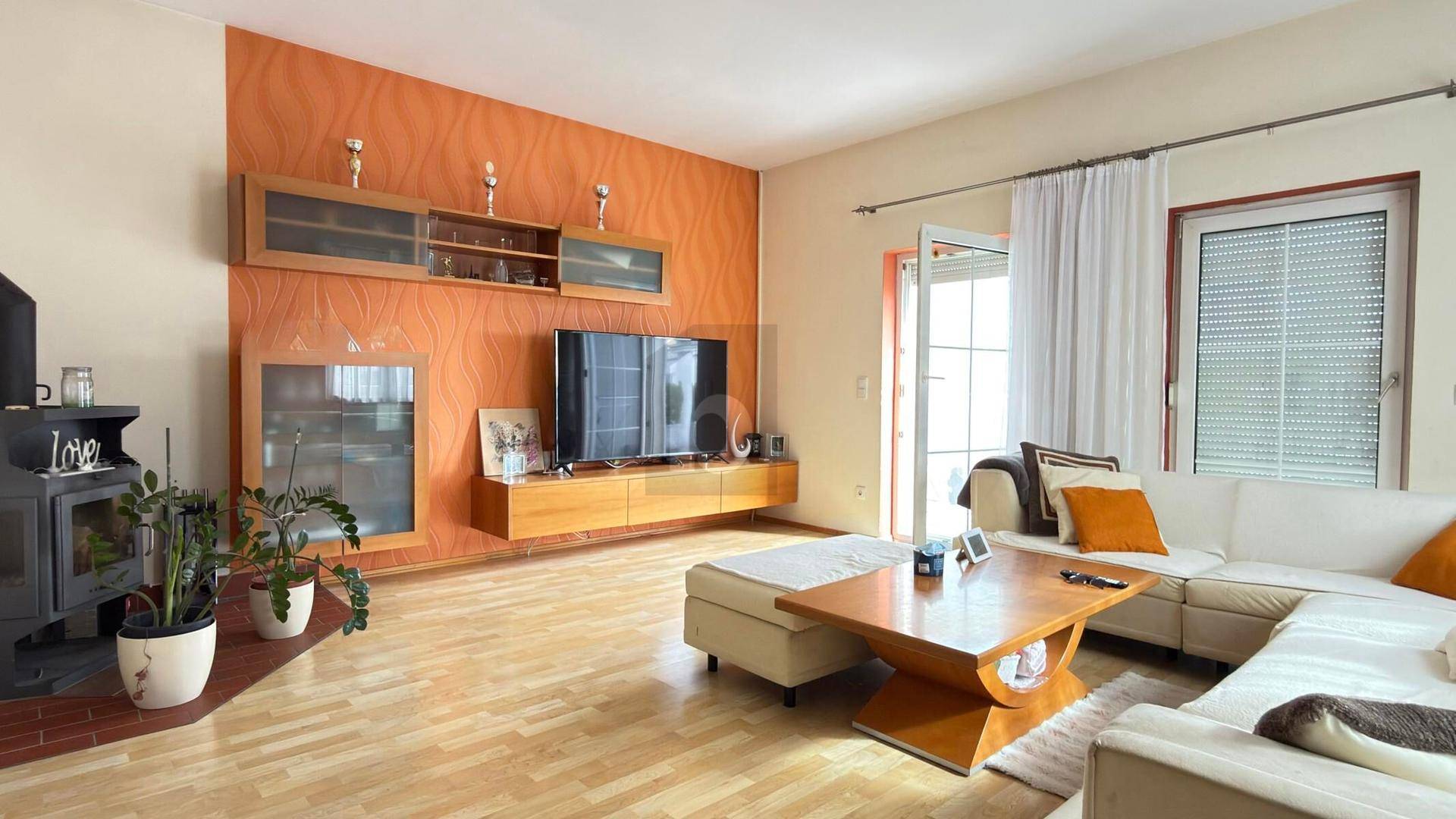 Gemütliches Wohnzimmer mit orangefarbener Akzentwand, Holzboden und Kaminofen.