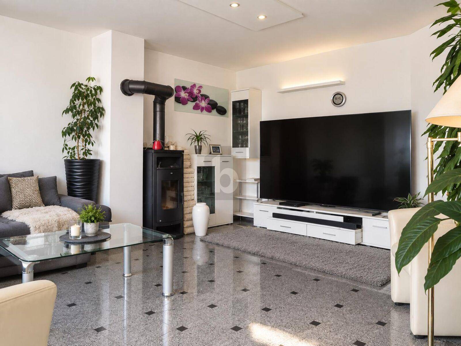 Gemütliches Wohnzimmer mit modernem Kaminofen, großem Fernseher und stilvollem Terrazzoboden.