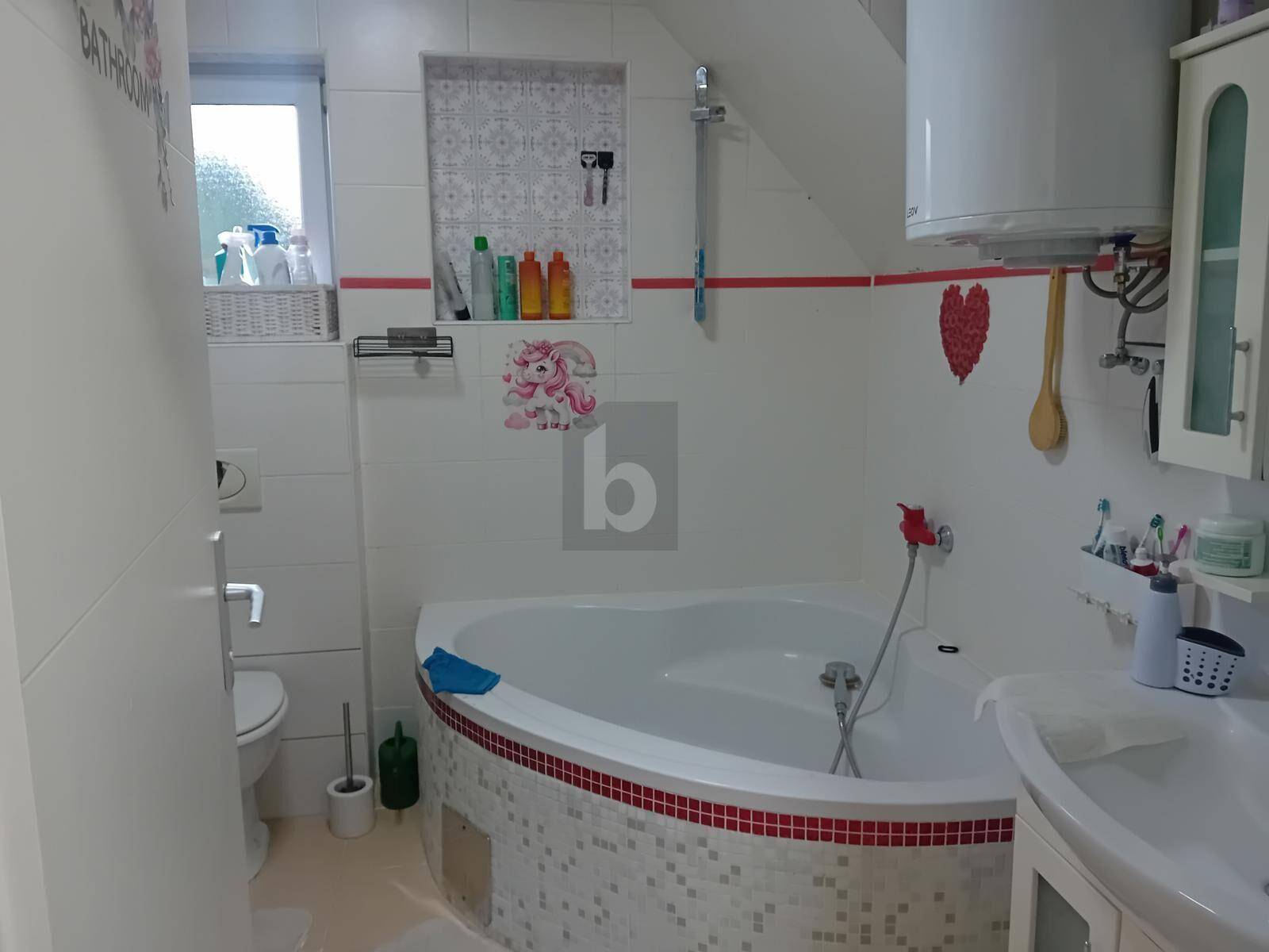 Helles Badezimmer mit weißen Fliesen, Eckbadewanne, WC und Fenster für Tageslicht.