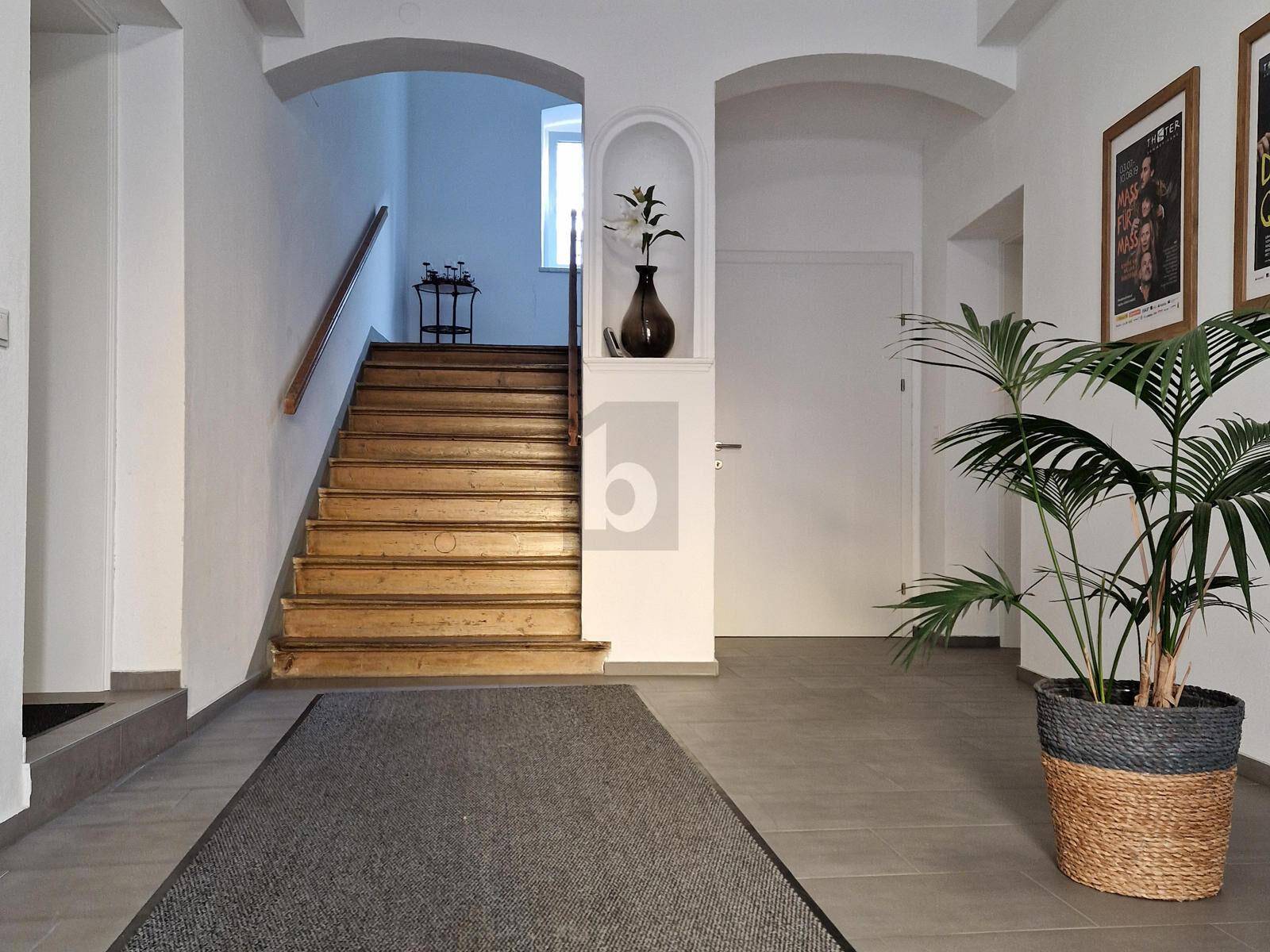 Heller Eingangsbereich mit Holztreppe, Fliesenboden und dekorativen Pflanzen.