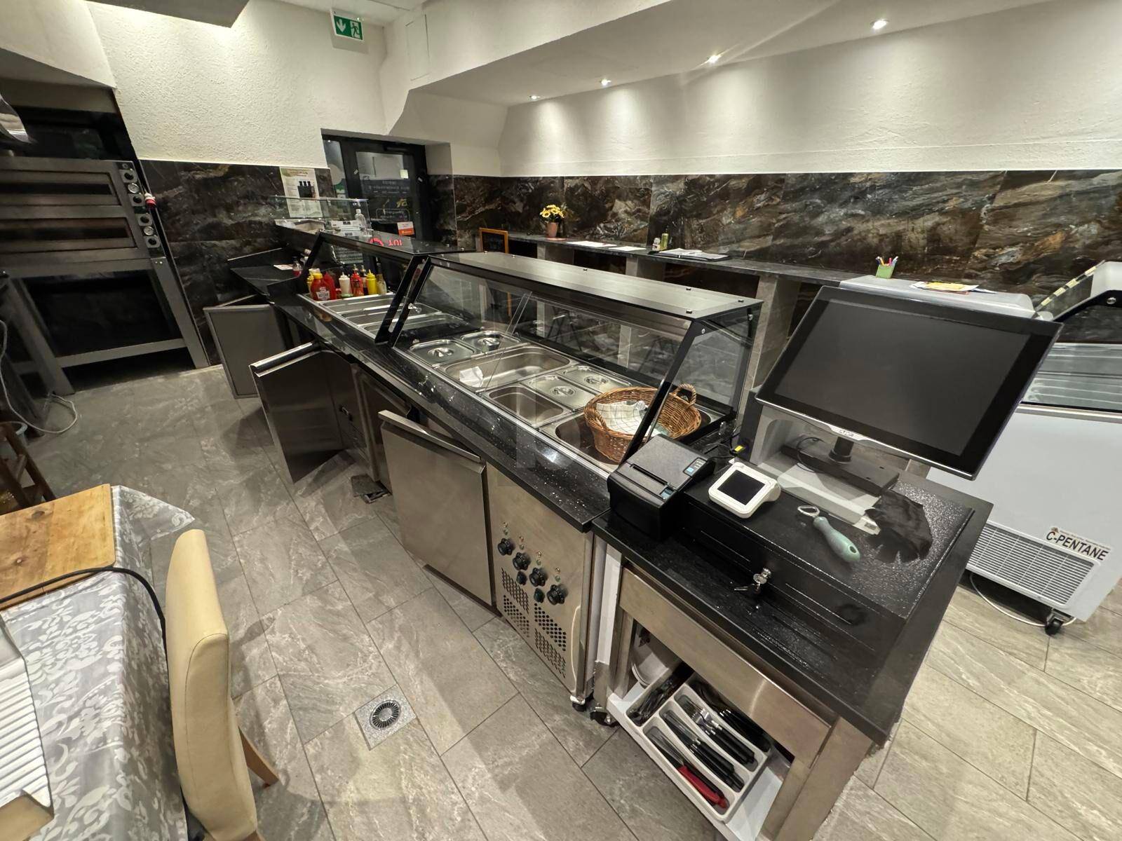Funktionale Servicetheke mit Kassensystem und Kühlvitrinen in einer professionellen Gewerbeküche mit Fliesenboden.