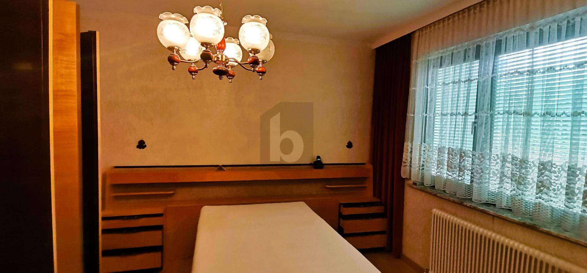 Schlafzimmer mit Doppelbett, Holzmöbeln und großem Fenster.