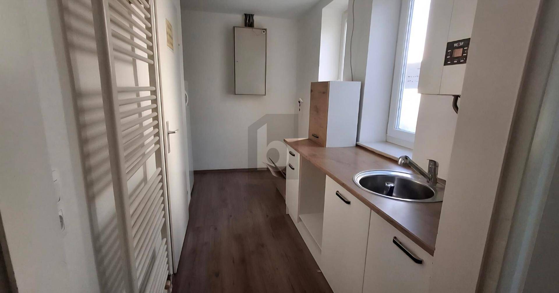 Kleine Küchenzeile mit Spüle, Holztheke und weißen Unterschränken, ergänzt durch ein Fenster und Handtuchheizkörper.