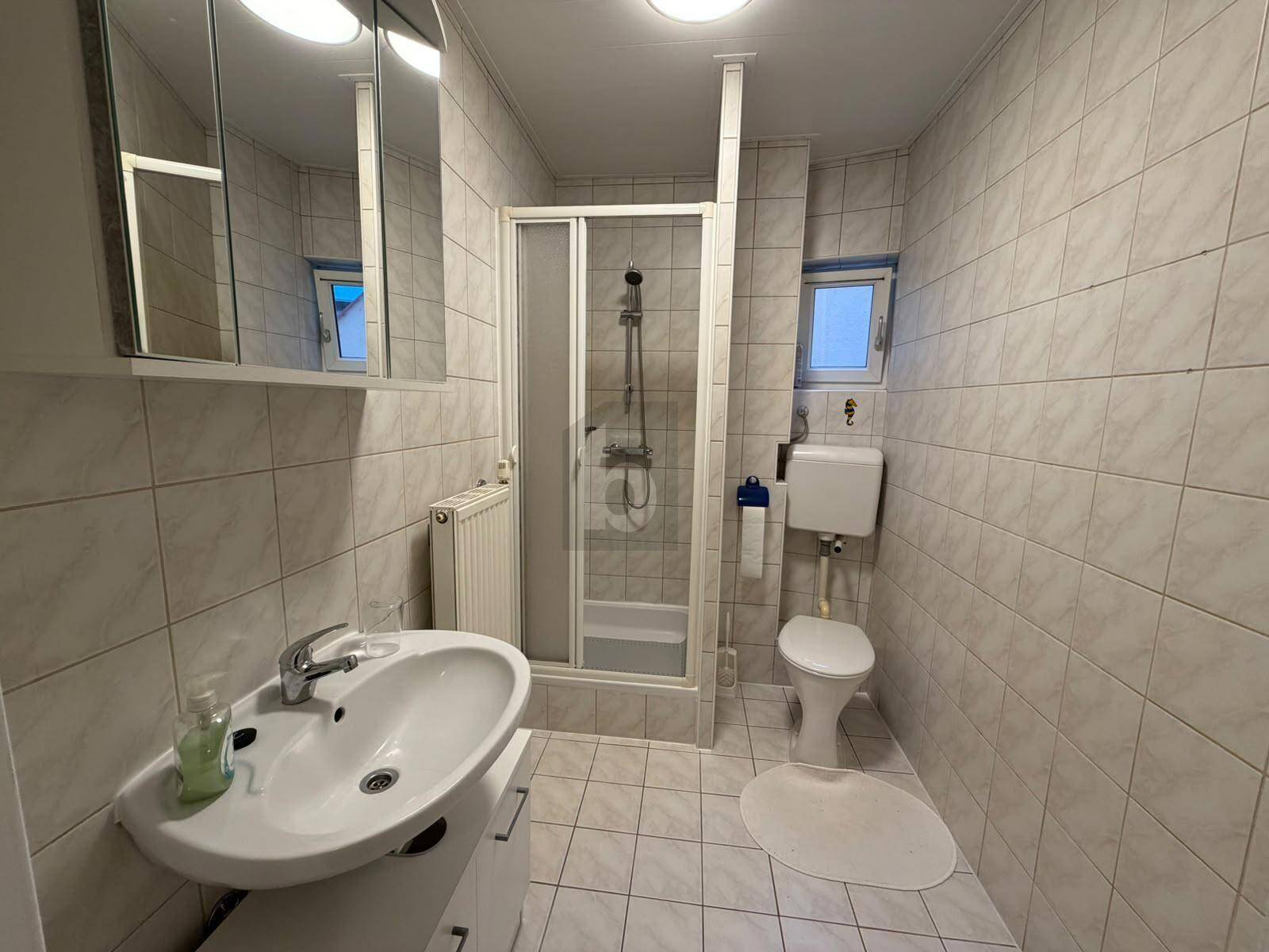 Gefliestes Badezimmer mit Dusche, WC, Waschbecken und Spiegelschrank in hellem Design.