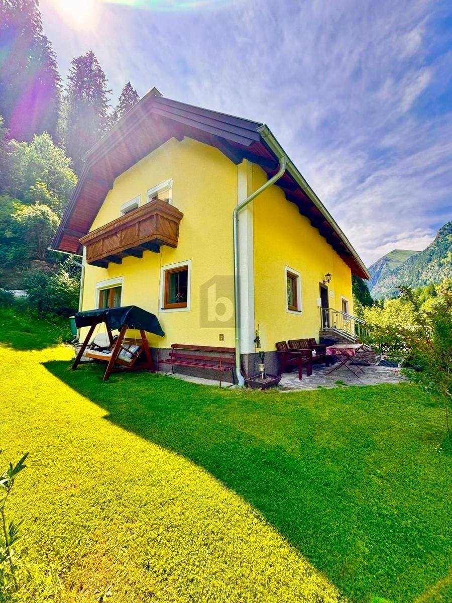 Charmantes gelbes Haus mit Holzbalkon, Schaukel und Sitzgelegenheiten im grünen Garten.