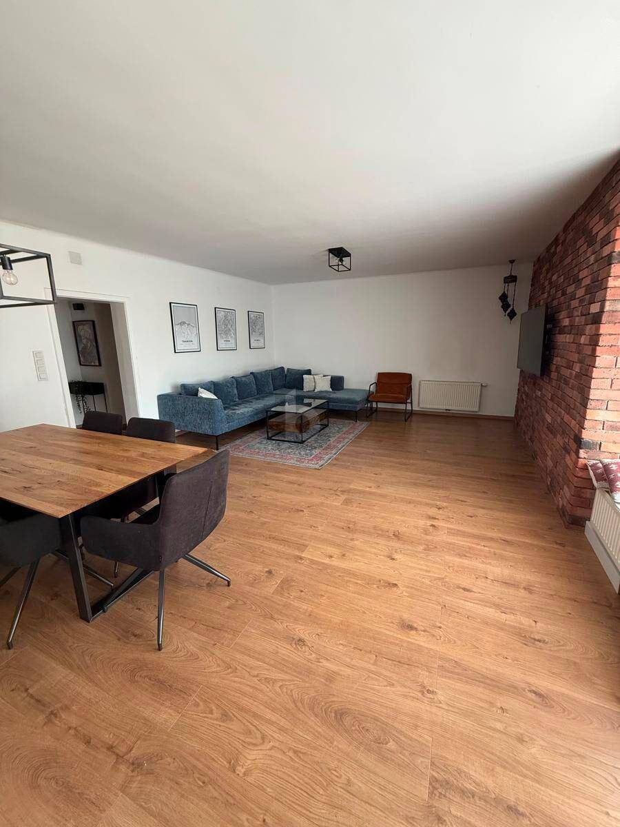 Offener Wohn- und Essbereich mit Laminatboden, freiliegender Ziegelwand und modernem Sofa.