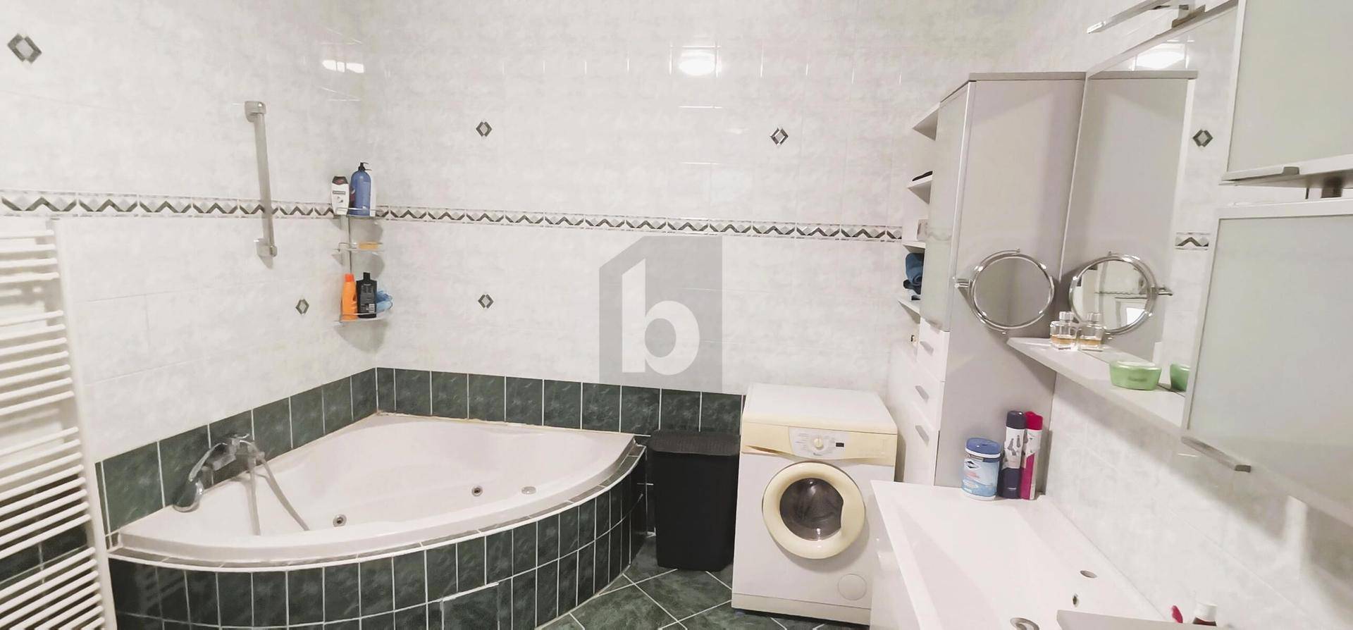 Badezimmer mit Eckbadewanne, Waschmaschine und grün-weißen Fliesen an Wänden und Boden.