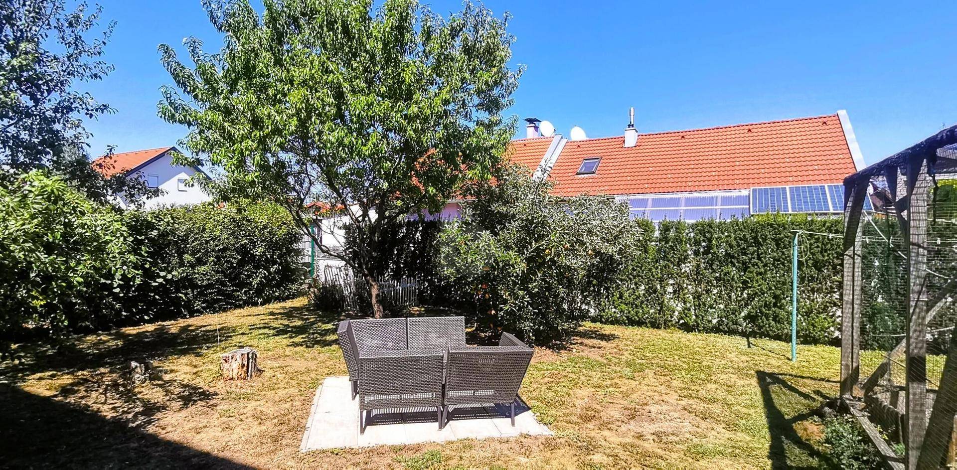 Grüner Gartenbereich mit Sitzgelegenheiten, Rasenfläche und hohen Hecken im Hintergrund.
