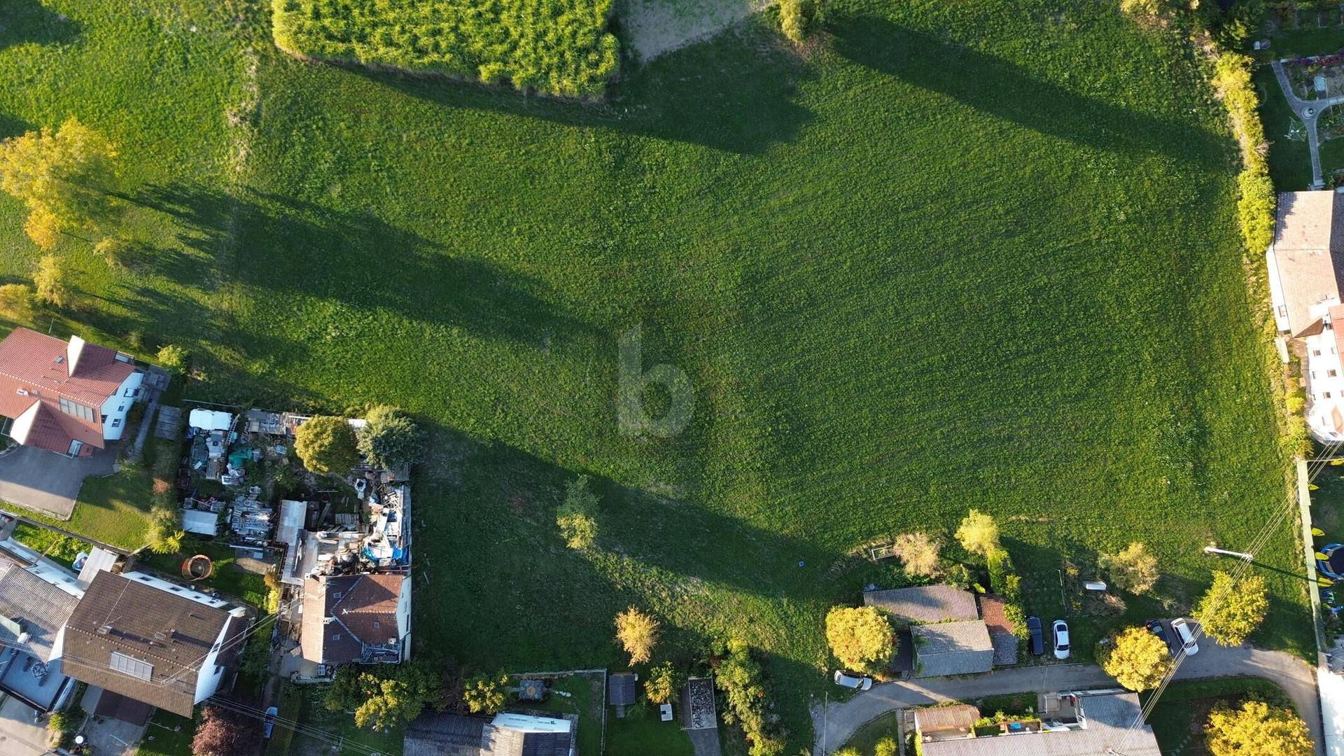 Panoramablick von oben auf ein großes, unbebautes Feld mit umliegenden Häusern und Gärten.