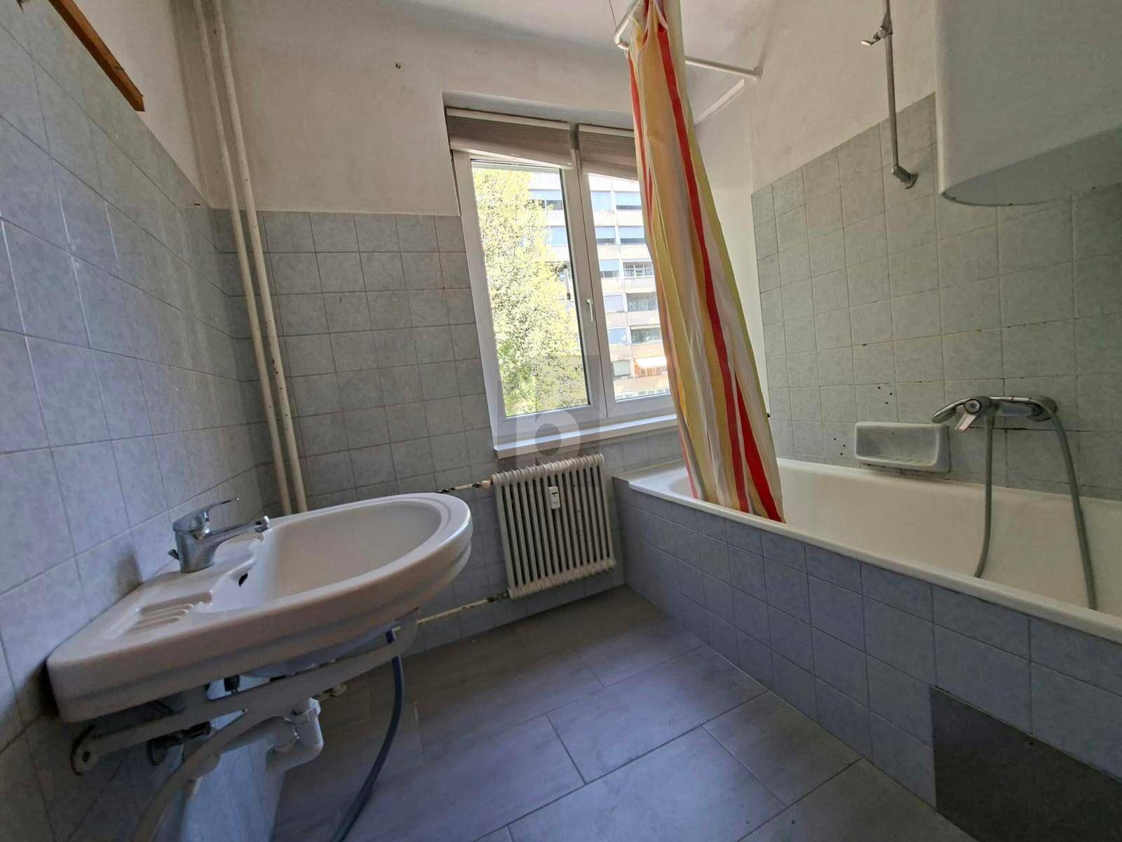 Badezimmer mit hellblauen Fliesen, Badewanne mit Duschvorhang und Fenster.