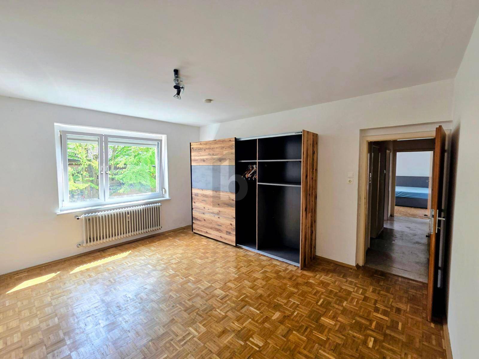 Helles Schlafzimmer mit Parkettboden, großem Fenster und modernem Kleiderschrank.